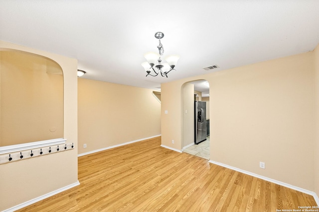 empty room featuring visible vents, arched walkways, baseboards, light wood finished floors, and a chandelier