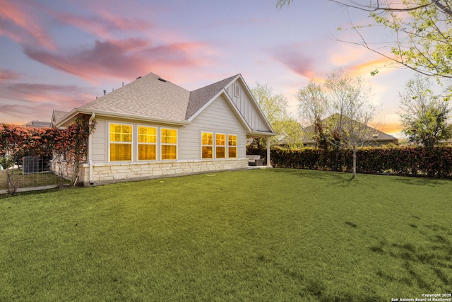 rear view of property with board and batten siding, a lawn, fence, a shingled roof, and stone siding