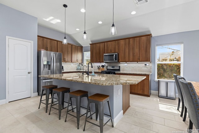 kitchen featuring appliances with stainless steel finishes, a breakfast bar, a sink, decorative backsplash, and visible vents