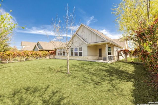 back of house featuring board and batten siding, a lawn, a fenced backyard, and stone siding