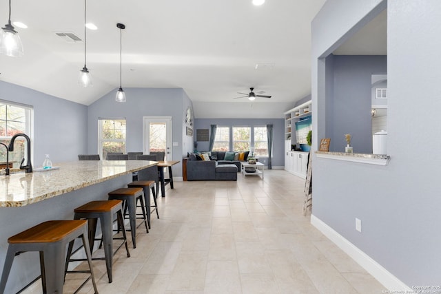 kitchen with ceiling fan, a kitchen bar, visible vents, light stone countertops, and lofted ceiling