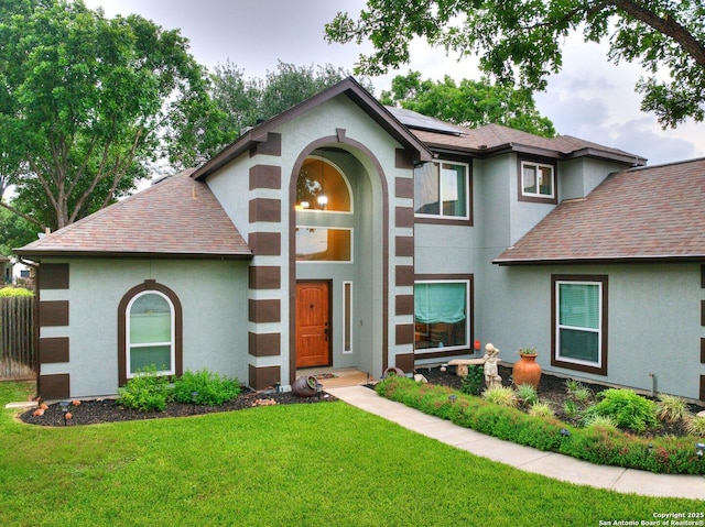 view of front of home featuring roof mounted solar panels, a shingled roof, stucco siding, and a front yard