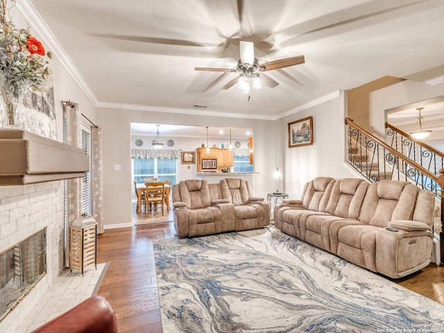 living room featuring ornamental molding, wood finished floors, a fireplace, ceiling fan, and stairway
