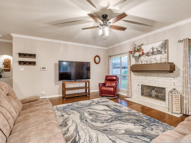 living area featuring a ceiling fan, a brick fireplace, wood finished floors, and ornamental molding