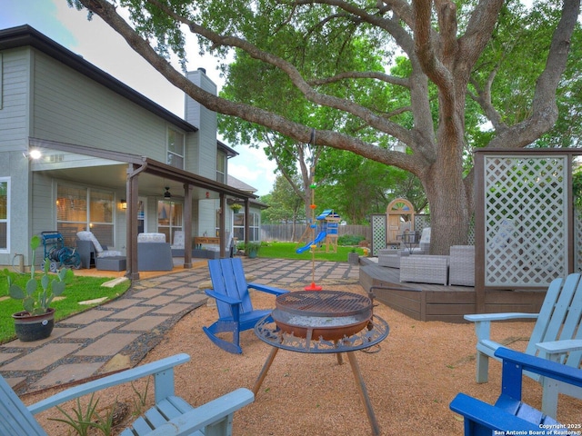 view of patio with a playground, a ceiling fan, an outdoor fire pit, and fence