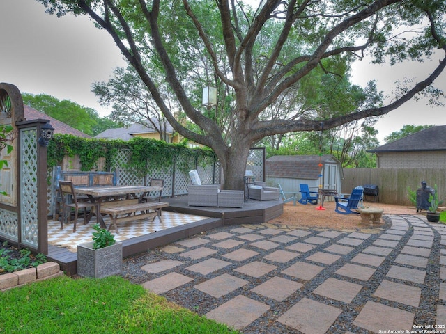 view of patio featuring a deck, a fenced backyard, a storage unit, an outbuilding, and outdoor dining space