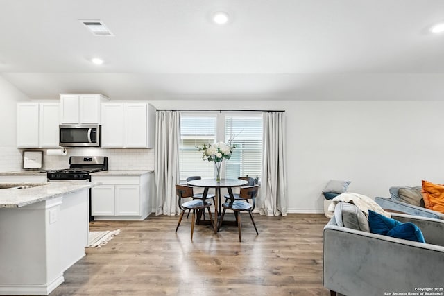 kitchen featuring appliances with stainless steel finishes, light stone counters, light wood finished floors, decorative backsplash, and visible vents
