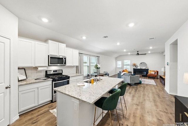 kitchen with decorative backsplash, a ceiling fan, appliances with stainless steel finishes, light wood finished floors, and lofted ceiling