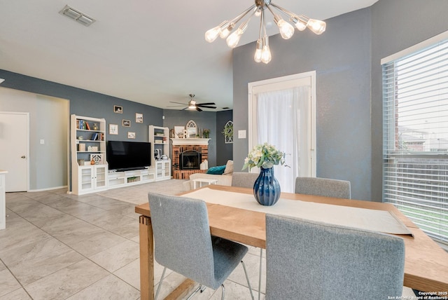 dining area featuring ceiling fan with notable chandelier, a brick fireplace, and visible vents