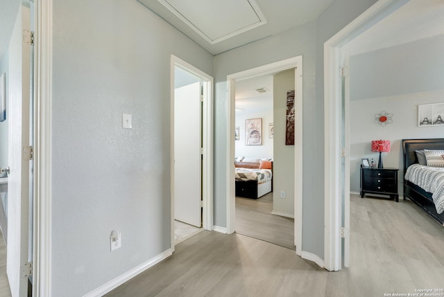 hallway with attic access, baseboards, visible vents, and light wood finished floors