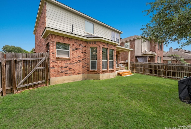 rear view of property featuring brick siding, a fenced backyard, a yard, and a gate