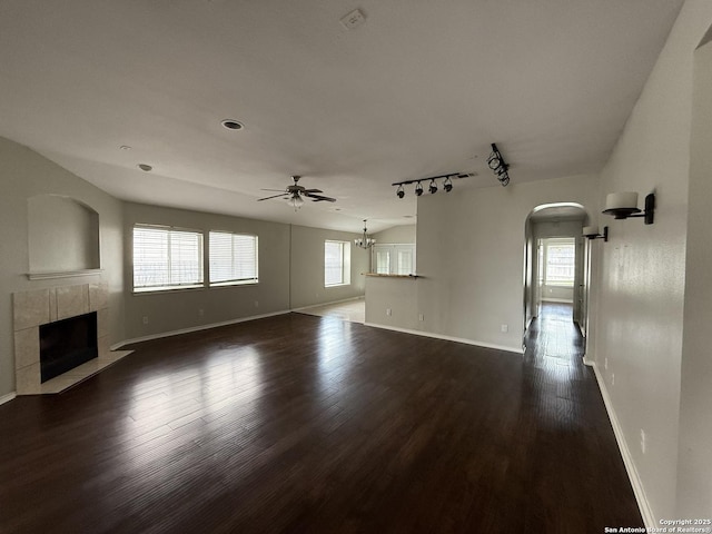 unfurnished living room with ceiling fan, baseboards, dark wood-type flooring, and a tile fireplace