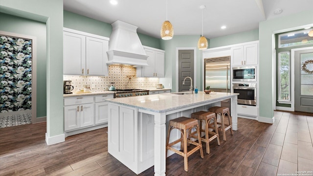 kitchen with decorative backsplash, built in appliances, custom exhaust hood, dark wood-style floors, and white cabinetry