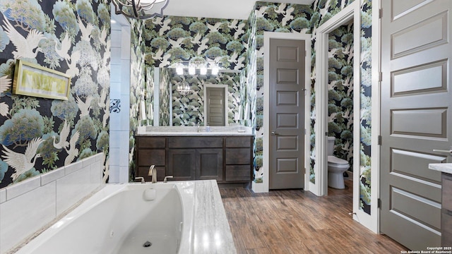 bathroom with a bath, wood finished floors, vanity, toilet, and wallpapered walls