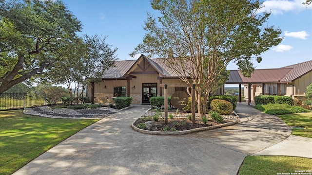 craftsman-style home featuring a standing seam roof, french doors, metal roof, fence, and stone siding