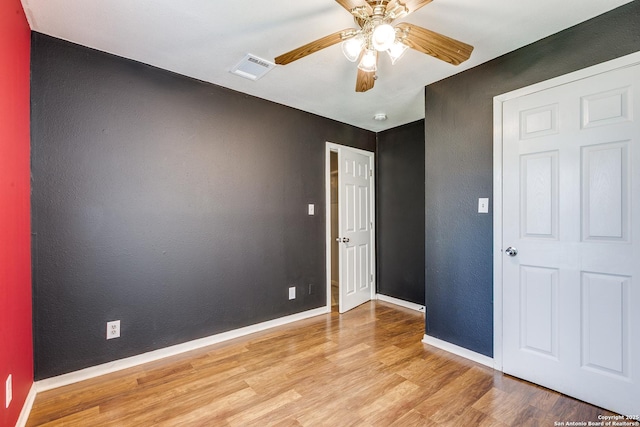 unfurnished room featuring a ceiling fan, visible vents, wood finished floors, baseboards, and a textured wall