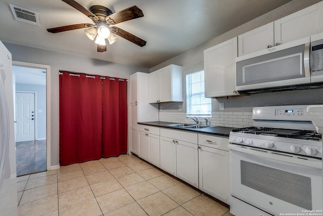 kitchen with dark countertops, a sink, white gas range, stainless steel microwave, and visible vents