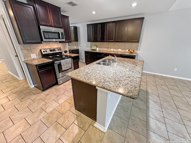 kitchen featuring decorative backsplash, visible vents, appliances with stainless steel finishes, a sink, and light stone counters