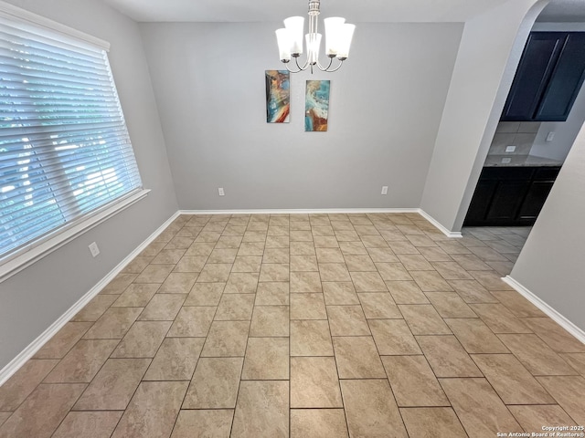 unfurnished dining area with arched walkways, baseboards, a notable chandelier, and light tile patterned floors