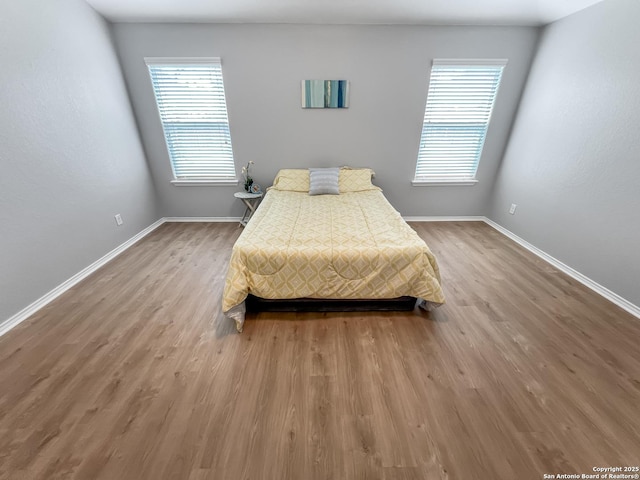 bedroom featuring baseboards, multiple windows, and wood finished floors