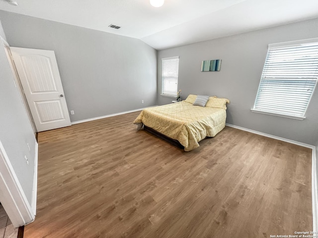 bedroom with baseboards, vaulted ceiling, wood finished floors, and visible vents