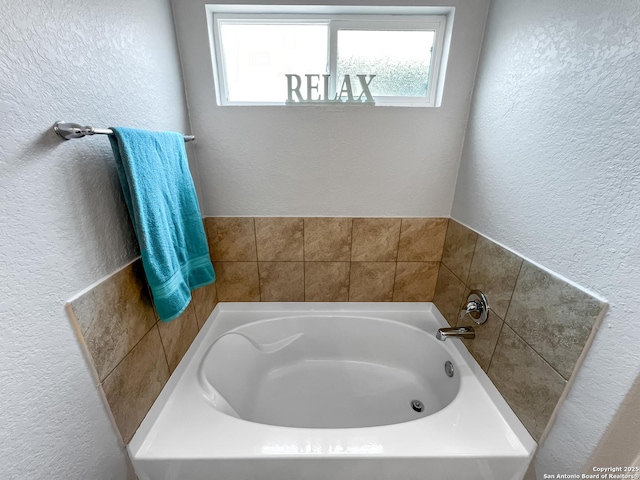 bathroom with plenty of natural light, a textured wall, and a bath