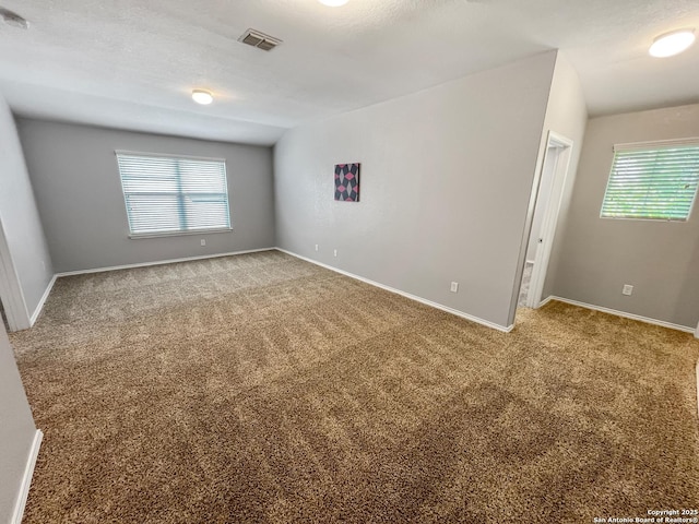 empty room with baseboards, carpet, vaulted ceiling, and visible vents