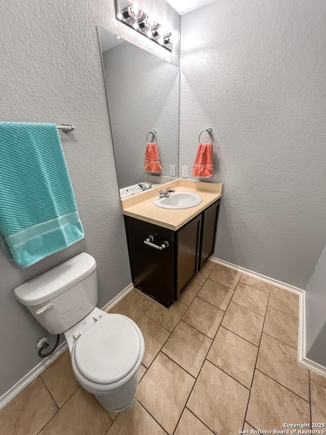 half bathroom with vanity, tile patterned flooring, a textured wall, and toilet