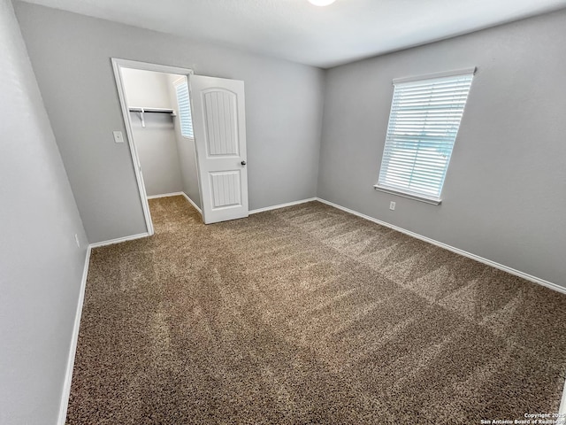 unfurnished bedroom featuring a closet, a walk in closet, baseboards, and carpet flooring