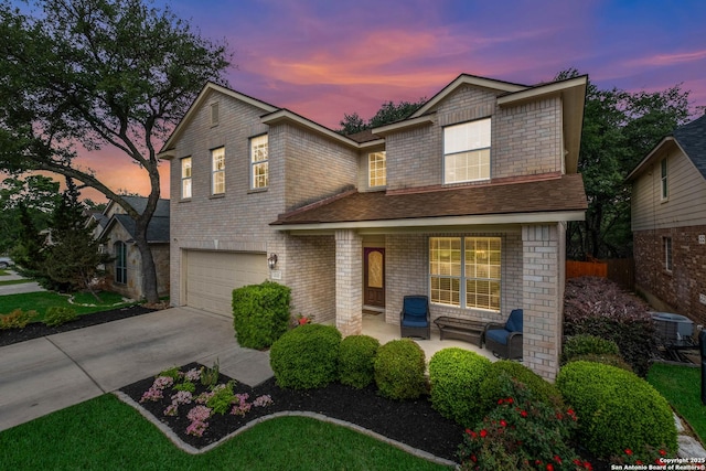 traditional-style house with a garage, covered porch, cooling unit, brick siding, and driveway