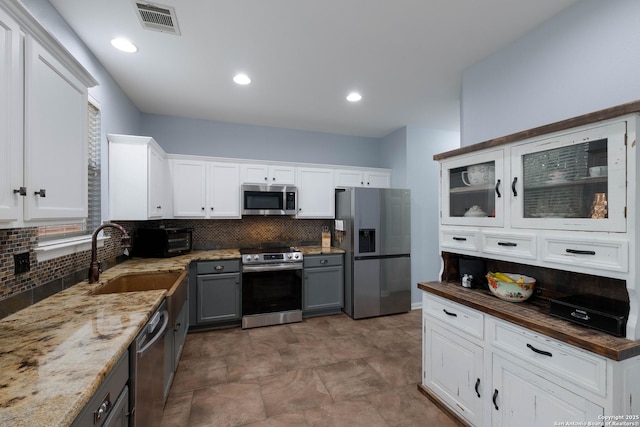kitchen featuring visible vents, gray cabinets, a sink, appliances with stainless steel finishes, and backsplash