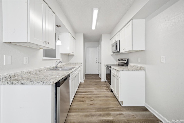 kitchen featuring appliances with stainless steel finishes, a sink, light countertops, white cabinets, and light wood-style flooring