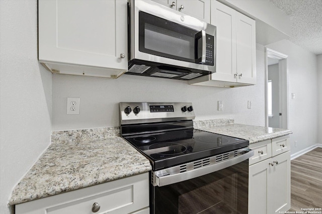 kitchen featuring a textured ceiling, appliances with stainless steel finishes, light stone countertops, white cabinets, and light wood-style floors