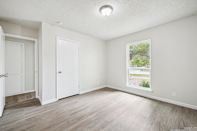unfurnished bedroom with a textured ceiling, baseboards, wood finished floors, and a closet