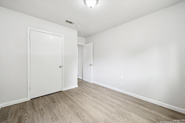unfurnished bedroom featuring light wood-style floors, baseboards, a textured ceiling, and visible vents