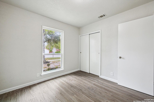 unfurnished bedroom with baseboards, wood finished floors, visible vents, and a closet