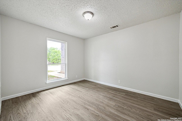 empty room featuring baseboards, dark wood finished floors, a textured ceiling, and visible vents