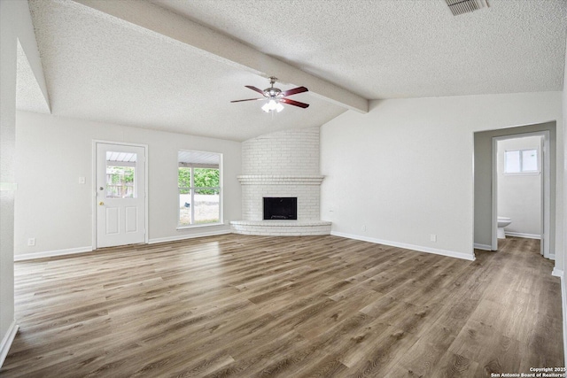 unfurnished living room with ceiling fan, a textured ceiling, visible vents, a fireplace, and wood finished floors