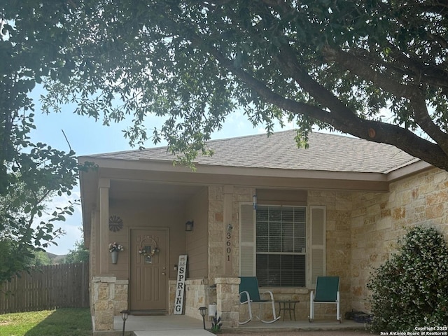 exterior space featuring roof with shingles, fence, and stone siding