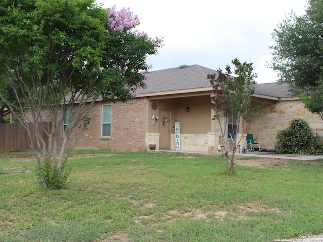 back of property featuring brick siding, roof with shingles, fence, and a yard