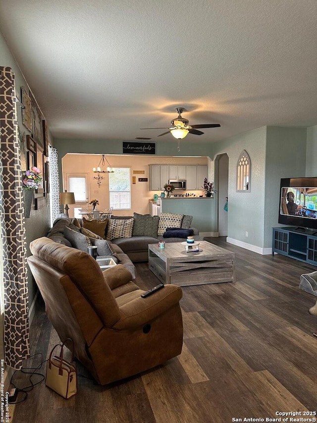 living room with dark wood-type flooring, arched walkways, baseboards, and ceiling fan with notable chandelier