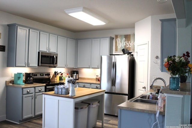 kitchen featuring gray cabinets, appliances with stainless steel finishes, a sink, butcher block counters, and dark wood-type flooring