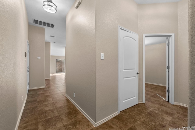 corridor featuring visible vents, baseboards, a textured wall, and tile patterned flooring