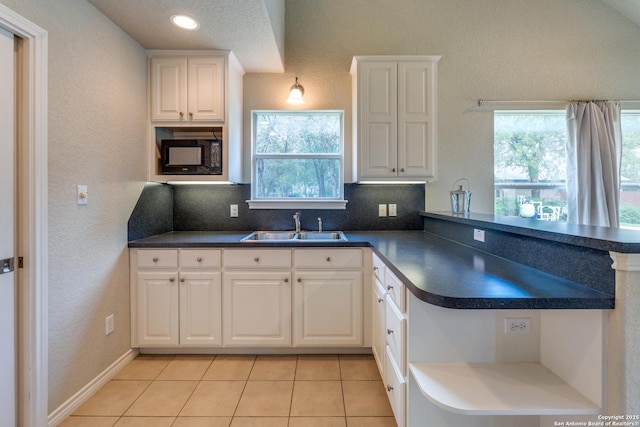 kitchen with black microwave, dark countertops, a sink, white cabinets, and a peninsula