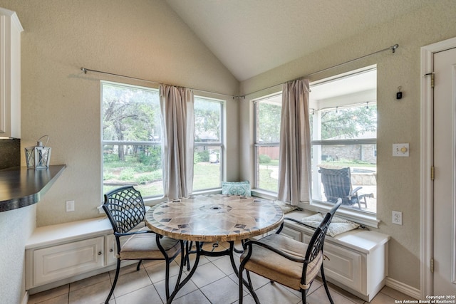 dining area with a textured wall, light tile patterned floors, lofted ceiling, and a wealth of natural light