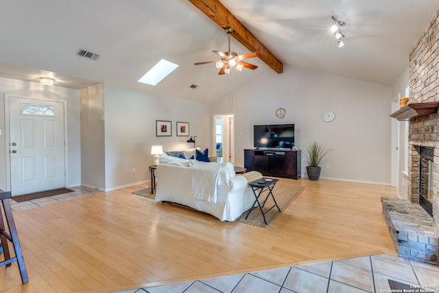 living area featuring ceiling fan, visible vents, a large fireplace, beam ceiling, and light wood-style flooring