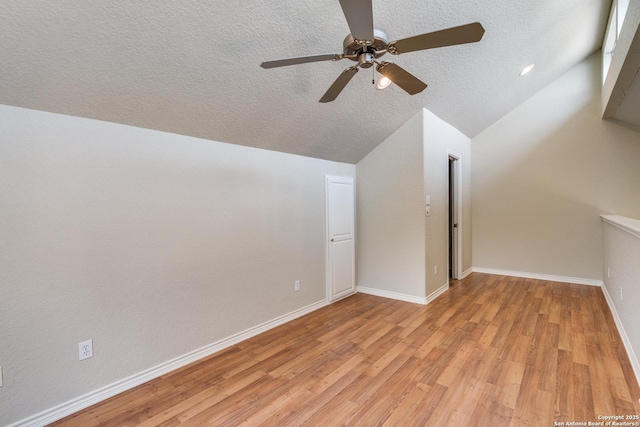 additional living space featuring a textured ceiling, light wood-style flooring, a ceiling fan, baseboards, and vaulted ceiling