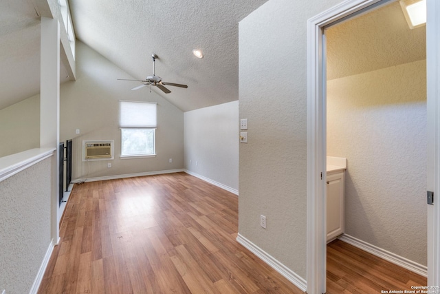 additional living space featuring a ceiling fan, baseboards, lofted ceiling, light wood-type flooring, and a wall mounted AC