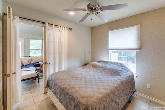 bedroom featuring baseboards, a ceiling fan, a textured wall, and light tile patterned floors