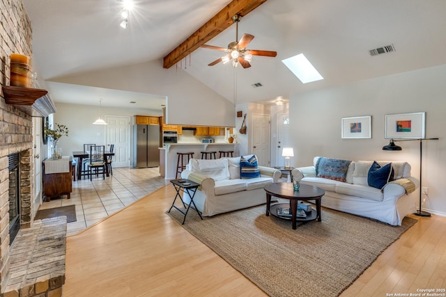 living room with visible vents, a brick fireplace, beamed ceiling, light wood-style floors, and ceiling fan